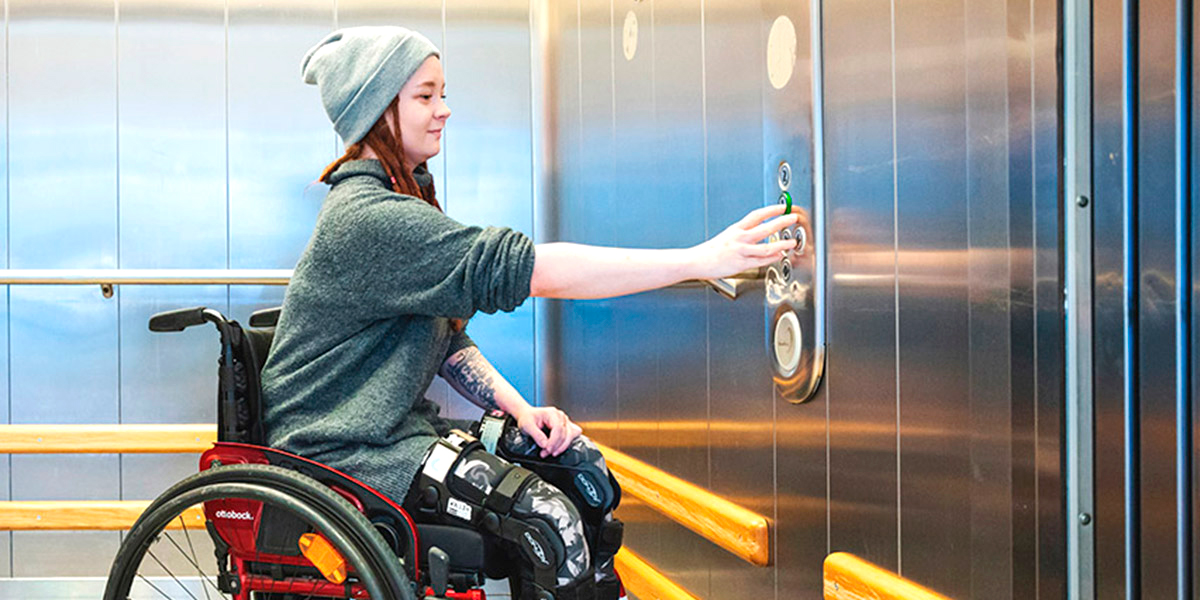 Nainen pyörätuolissa painaa hissin nappulaa
