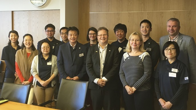 Kuvassa seisoo japanilaisia vieraita sekä invalidiliiton edustajia kokoustilassa.  