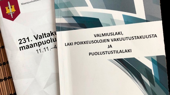 Valmiuslaki, Laki poikkeusolojen vakuutustakuusta ja puolustusilalaki-kirja ja sen takana osa Maanpuolustuskorkeakoulun kirjasta. Kuvituskuva.